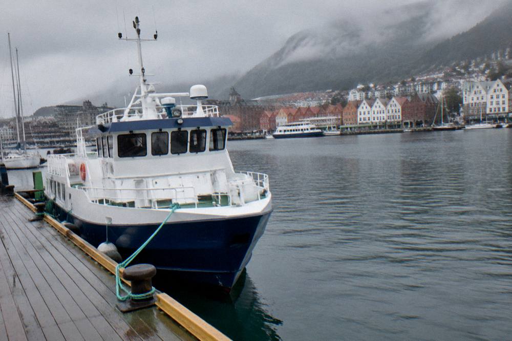 A fjord boat moored at a wooden pier in Bergen harbour in early morning light