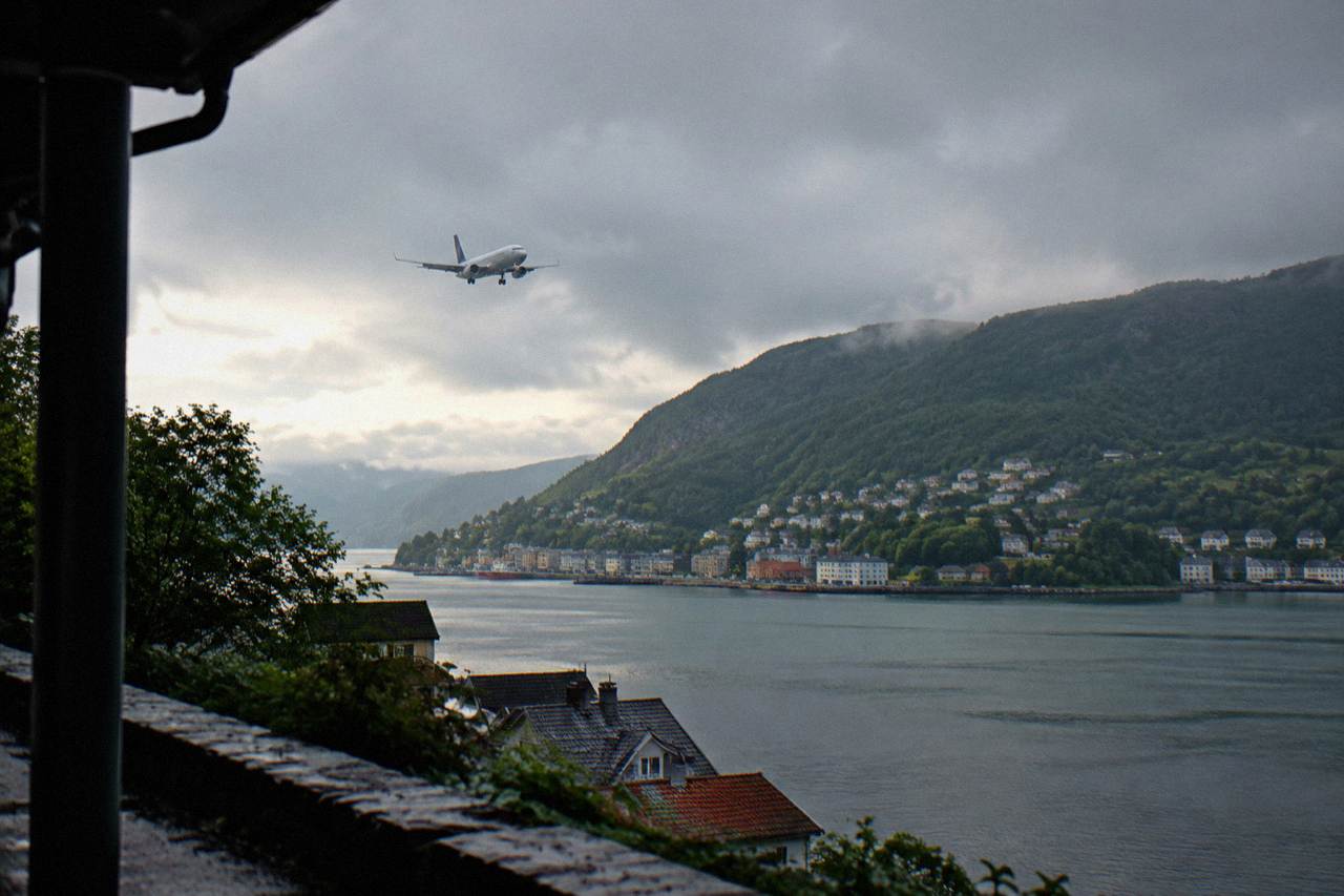 A passenger aircraft on approach over green hills and a fjord near Bergen