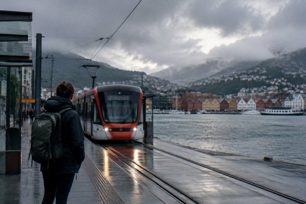 A traveller with a backpack watching a light rail tram arrive at a Bergen city stop