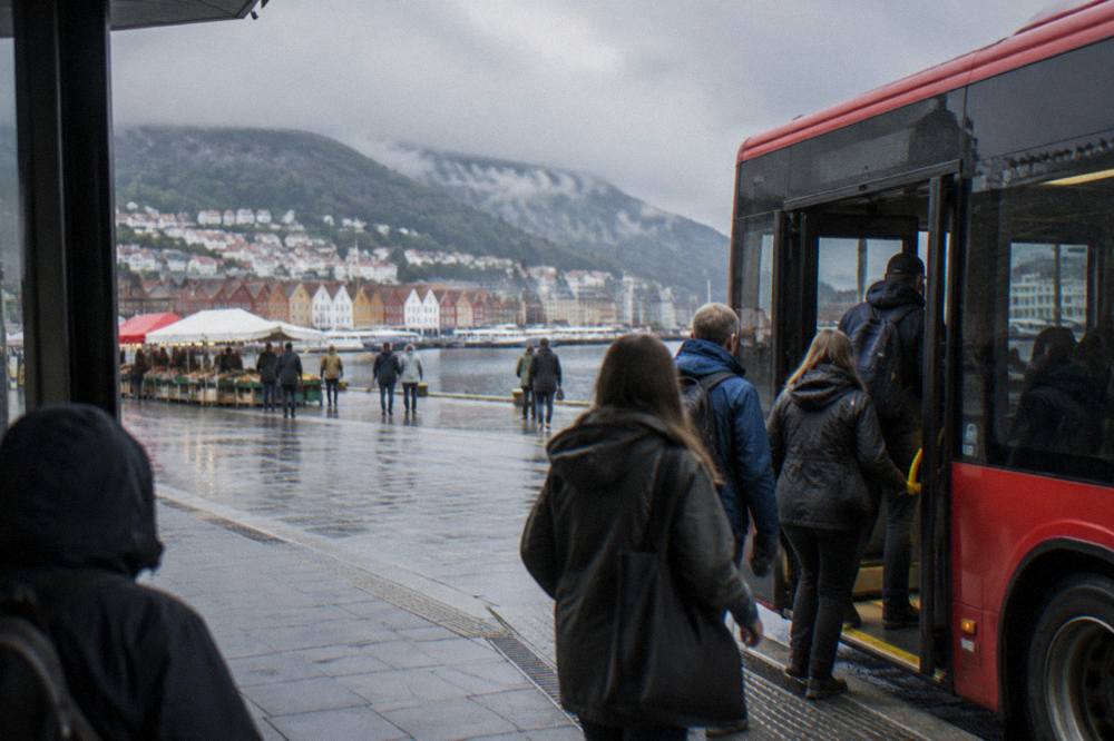 Passengers boarding a red city bus at a stop near a market square in Bergen