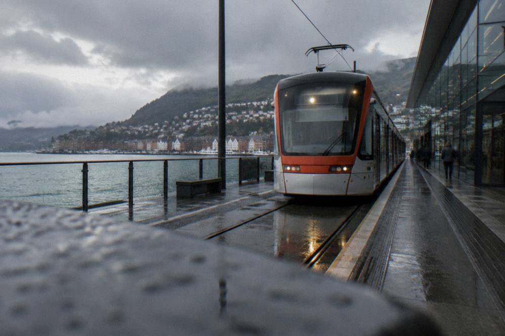 A light rail vehicle arriving at an outdoor platform stop beside a glass terminal building
