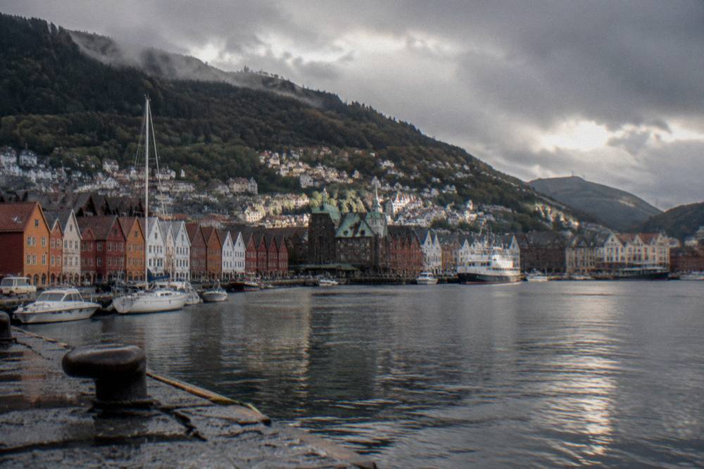 Evening light over the rooftops and harbour of Bergen with steep forested hills behind the city