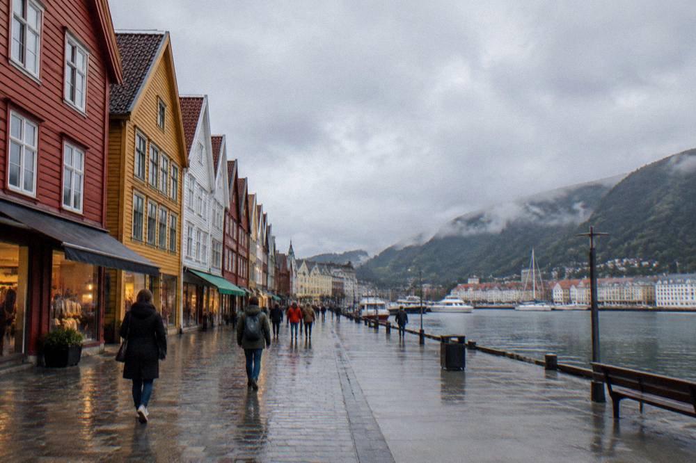 A pedestrian street in Bergen with people walking past colourful shopfronts on a bright day