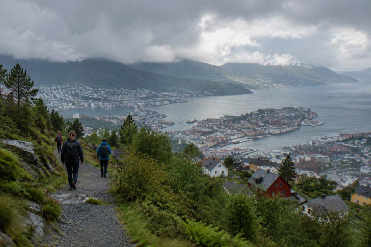 Hikers on a gravel trail above Bergen with wooden houses and the fjord below