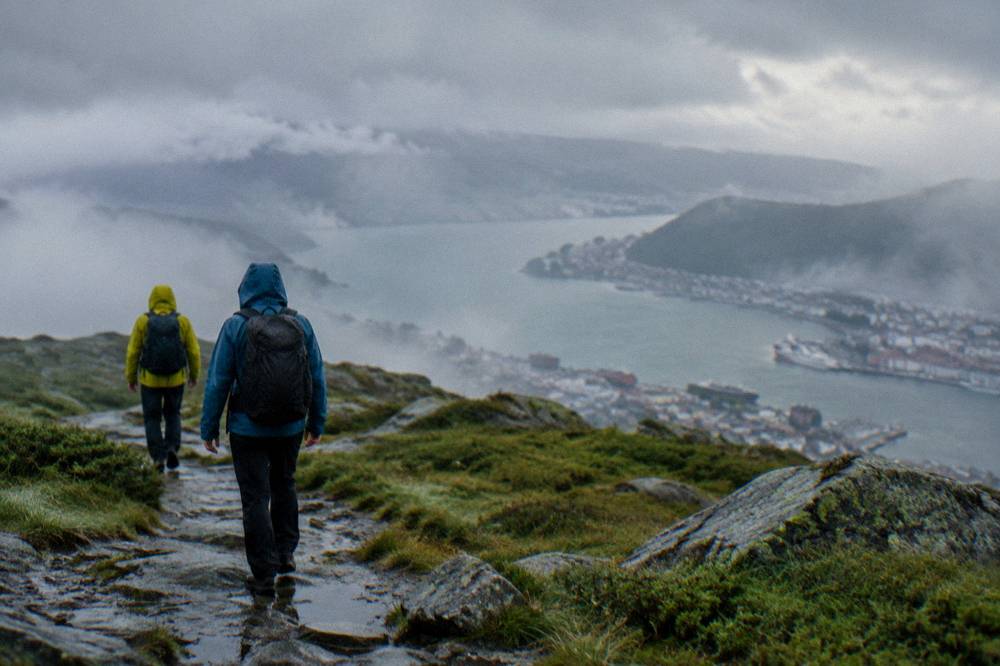 Two walkers in rain jackets crossing a misty mountain plateau near Bergen