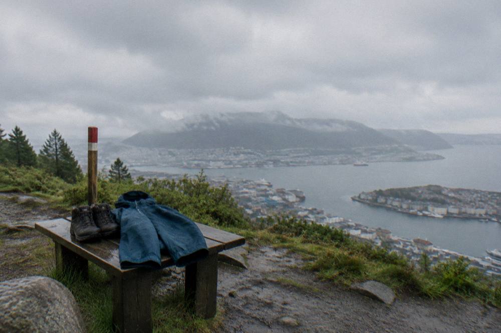 Hiking boots and a rain jacket resting on a bench beside a mountain trail marker