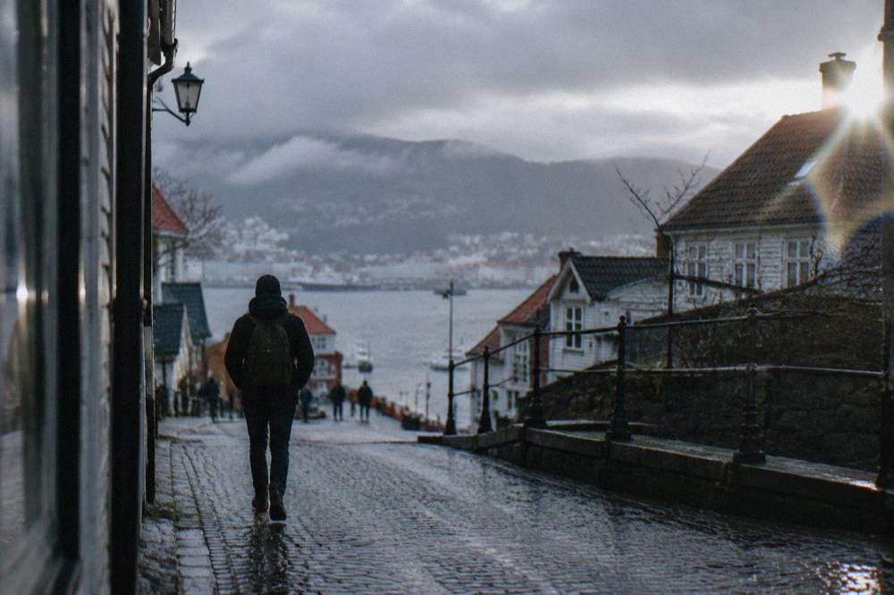 A lone walker with a backpack on a quiet cobblestone street in central Bergen