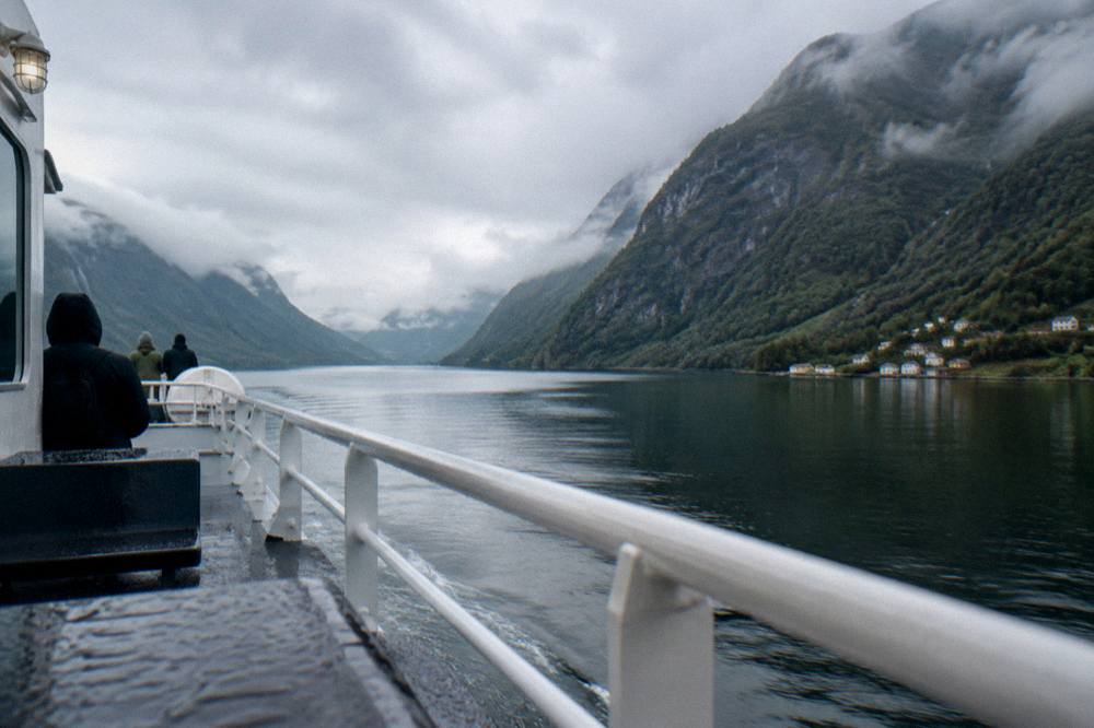 A passenger ferry crossing calm water between steep green cliffs in a Norwegian fjord