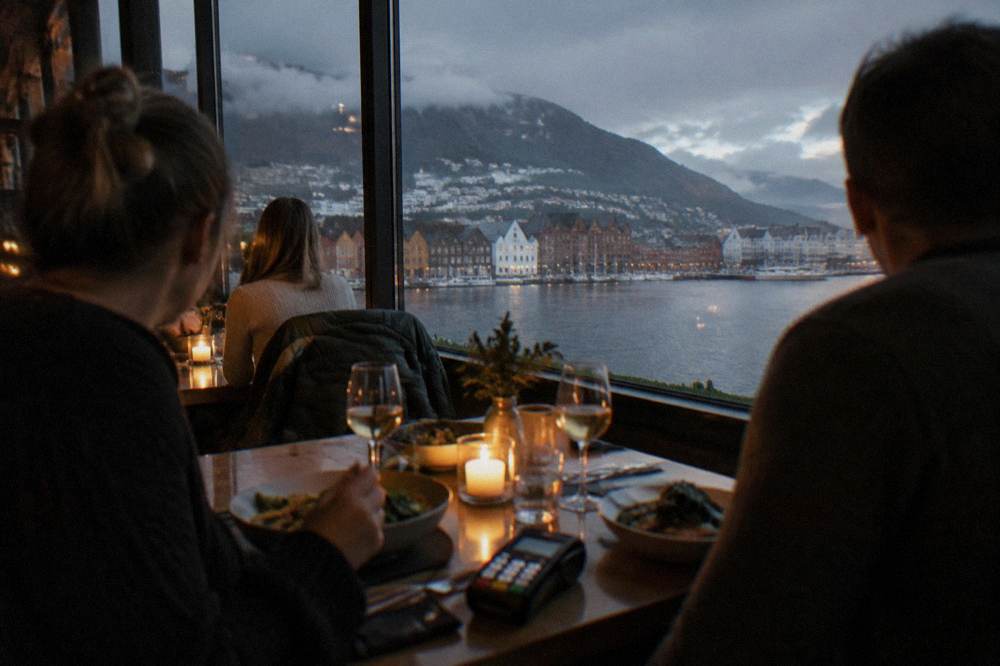 Diners sharing a meal at a candlelit table in a Bergen restaurant, a card terminal on the table