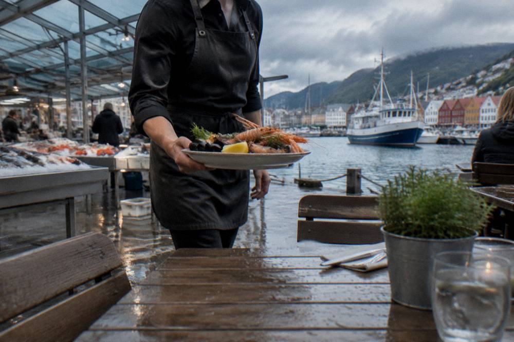 A waiter bringing a plate of fresh seafood to a table outside a restaurant near the Bergen fish market