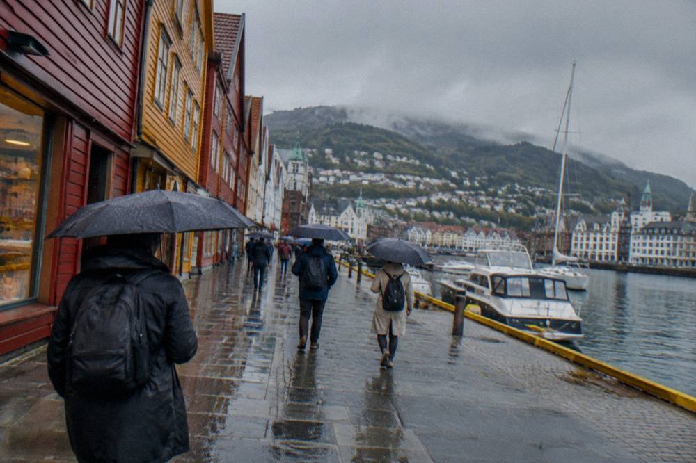 Visitors with umbrellas walking past shop fronts on a rainy street in central Bergen