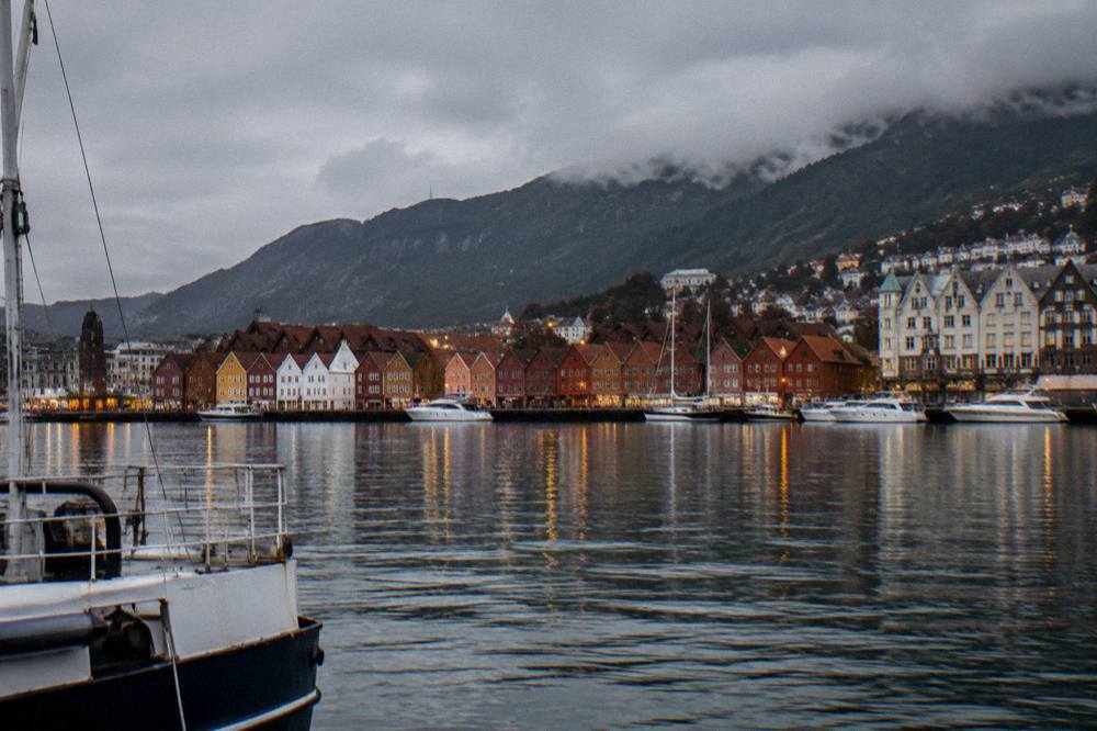 A harbour view of Bergen at dusk with mountain ridges behind the city and lights reflecting on the water