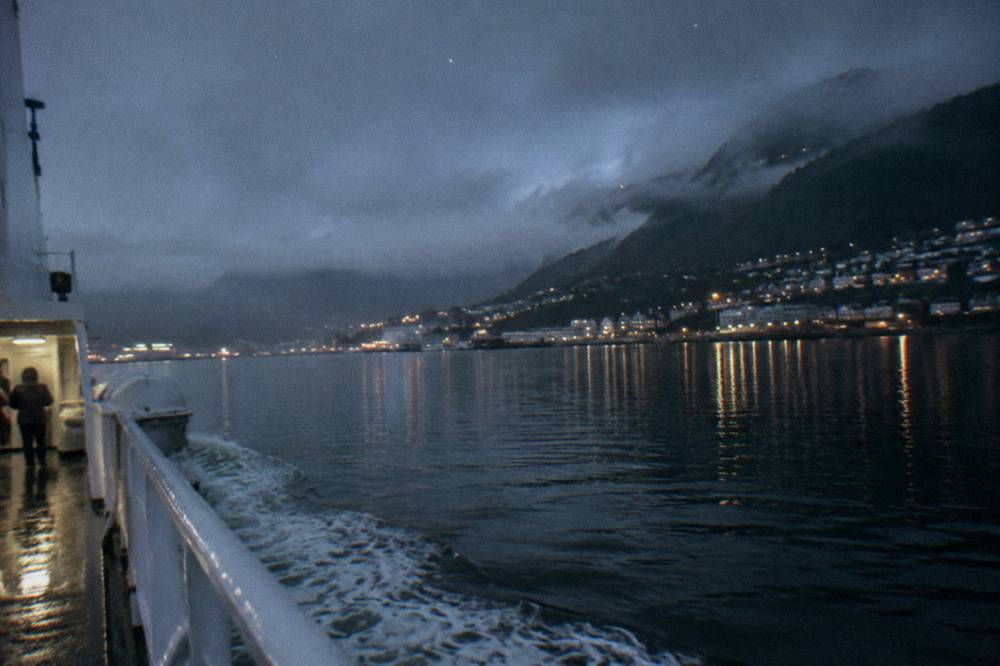 A night ferry crossing black fjord water beneath a faint star-filled sky
