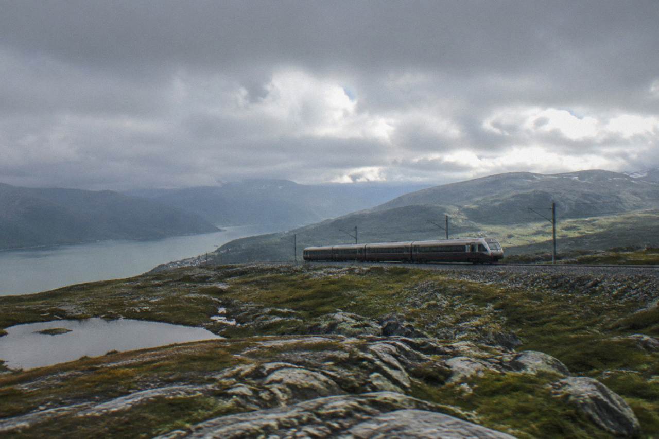 A passenger train crossing a bare mountain plateau in Norway under a low sky