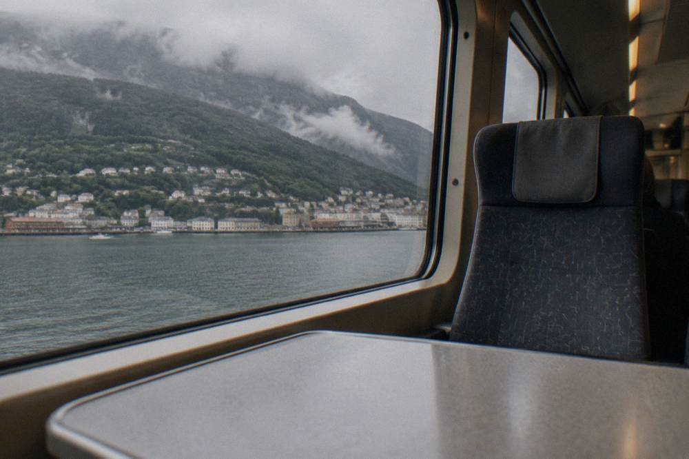 The interior of a Norwegian train carriage with large windows and reclined seats facing a mountain view