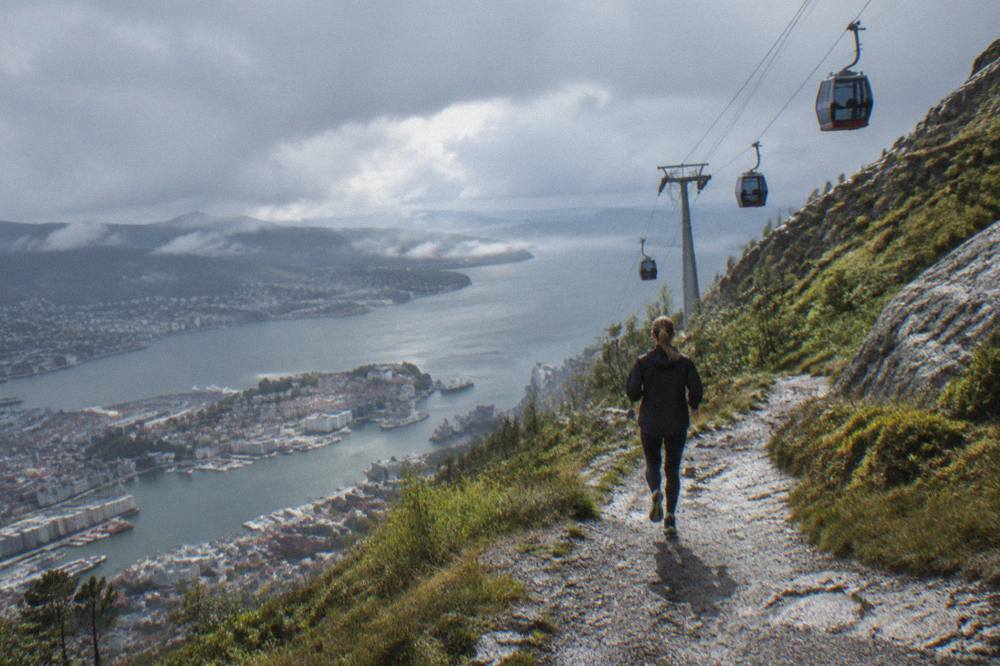 Cable car cabins climbing a steep granite mountain above Bergen with the city and fjord below