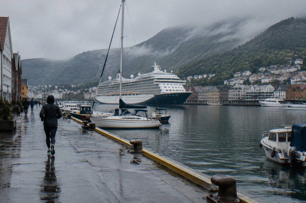 A cruise ship and small boats moored in Bergen's inner harbour with green mountains behind