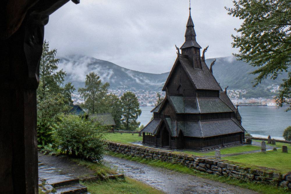 A wooden stave church with dark timber walls and tiered roofs standing among trees