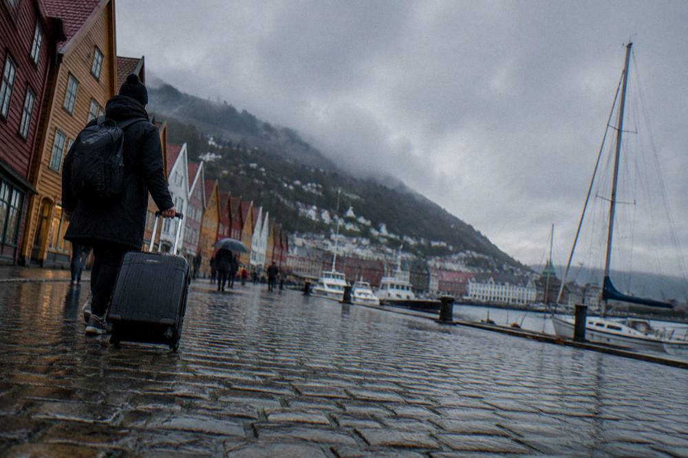 A traveler rolling a full suitcase across a wet cobblestone street in Bergen