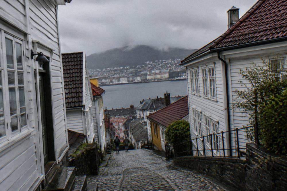 Steep cobbled lane with old wooden buildings rising up a hillside towards a mountain in Bergen