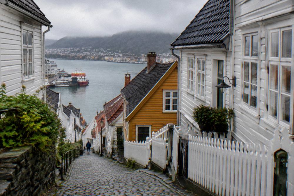 White wooden houses on a steep cobblestone lane in the Sandviken neighbourhood with the harbour below