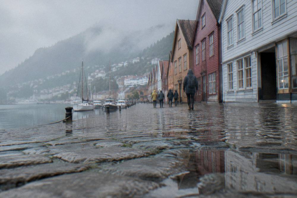 Wet cobblestone street in Bergen with rain jackets and reflections in puddles between old wooden buildings