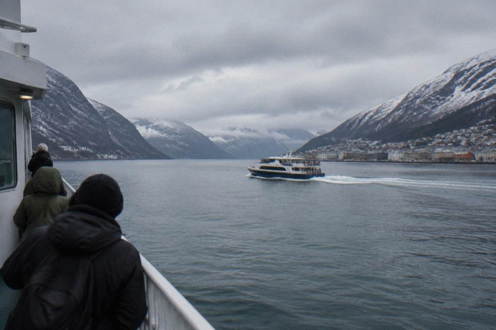 A tour boat crossing a calm Norwegian fjord with snow-dusted mountains on both sides