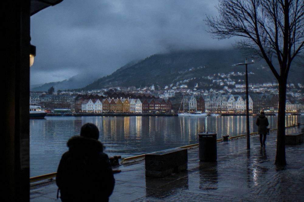 Bergen city lights reflecting in wet harbour water under a dark blue winter sky