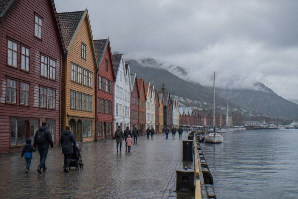 Families walking past the colourful gabled wooden buildings along the Bryggen wharf in Bergen