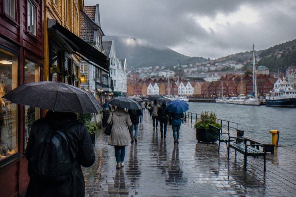 Visitors with umbrellas walking past shop fronts on a rainy street in central Bergen