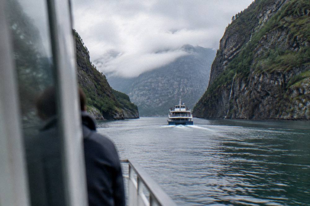 A small cruise boat heading up a narrow fjord with steep rocky walls near Bergen