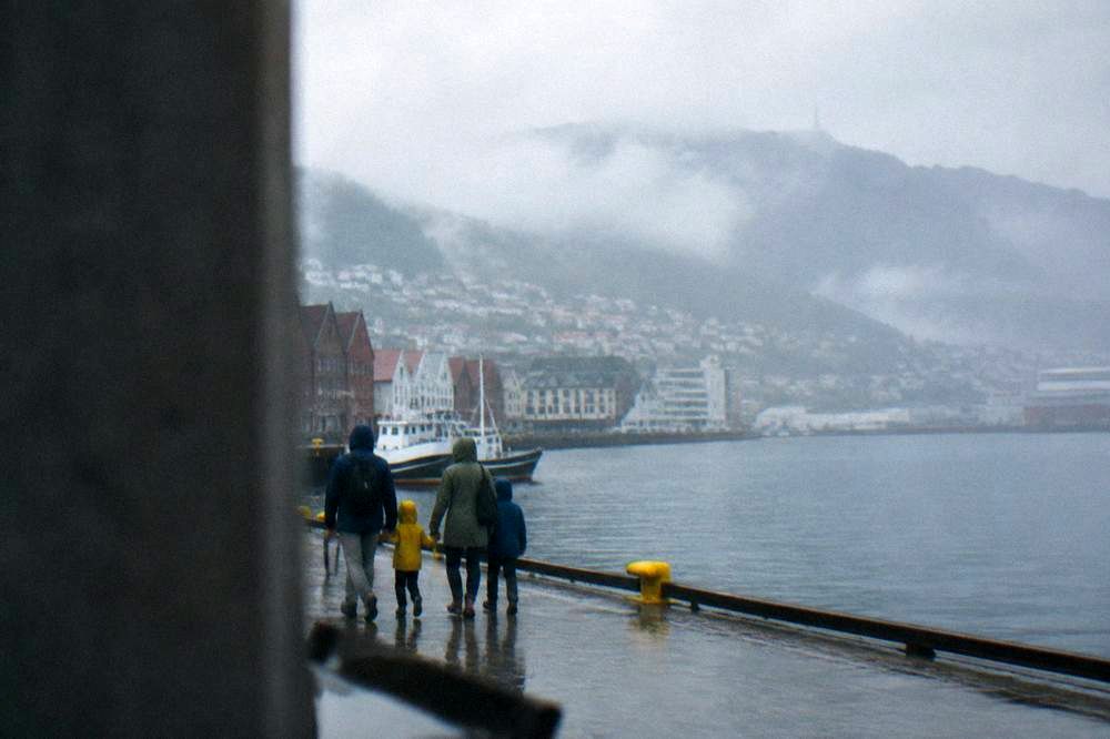 A family with rain jackets walking together along the harbourfront in Bergen with mountains behind