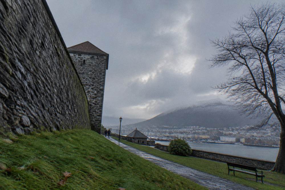 Stone walls of Bergenhus fortress with the harbour and green parkland around it on a grey day