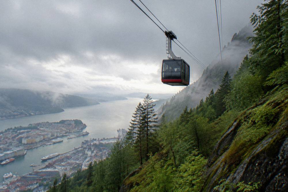 A cable car cabin ascending a misty green mountain above Bergen