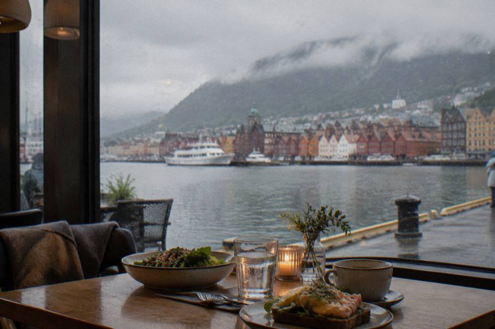 A table set for lunch inside a warm Bergen cafe with rain visible outside the window