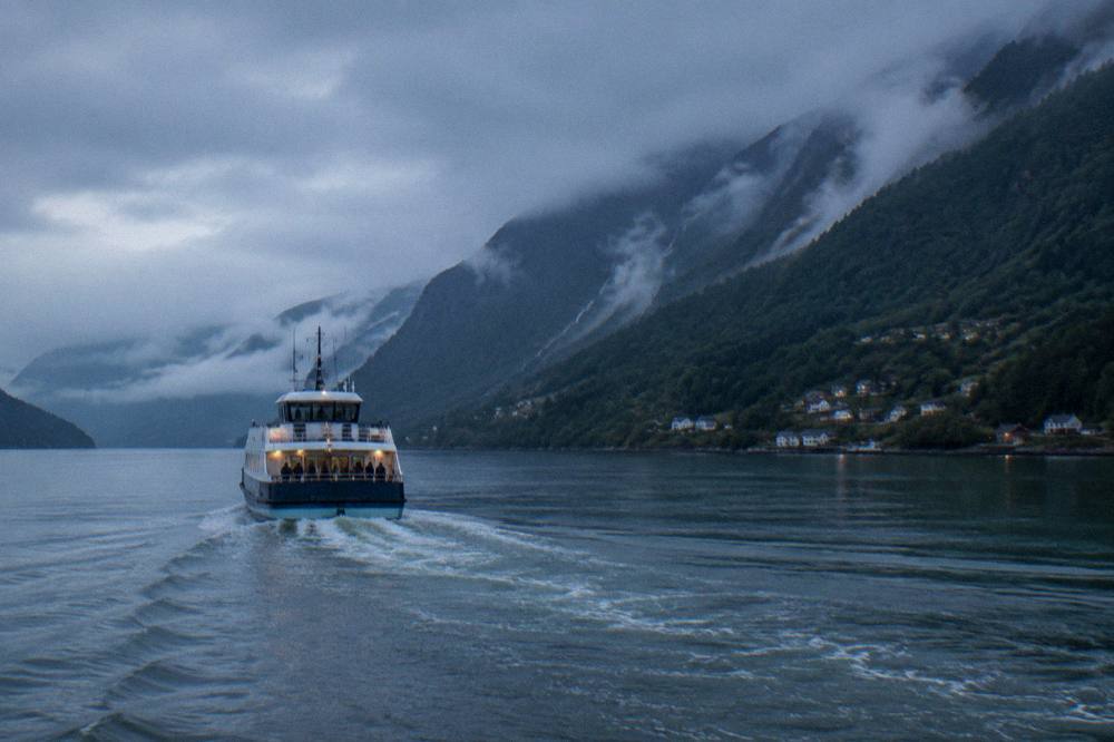 A passenger boat crossing the Hardangerfjord past steep forested slopes and low clouds
