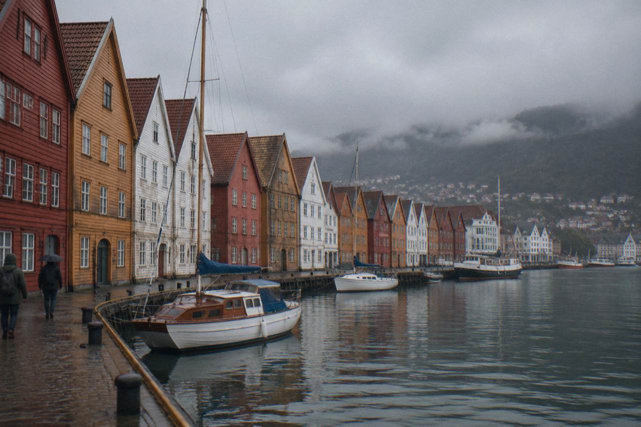 Colourful wooden Hanseatic buildings along the Bryggen wharf in Bergen, with small boats moored on the harbour water in front of them.
