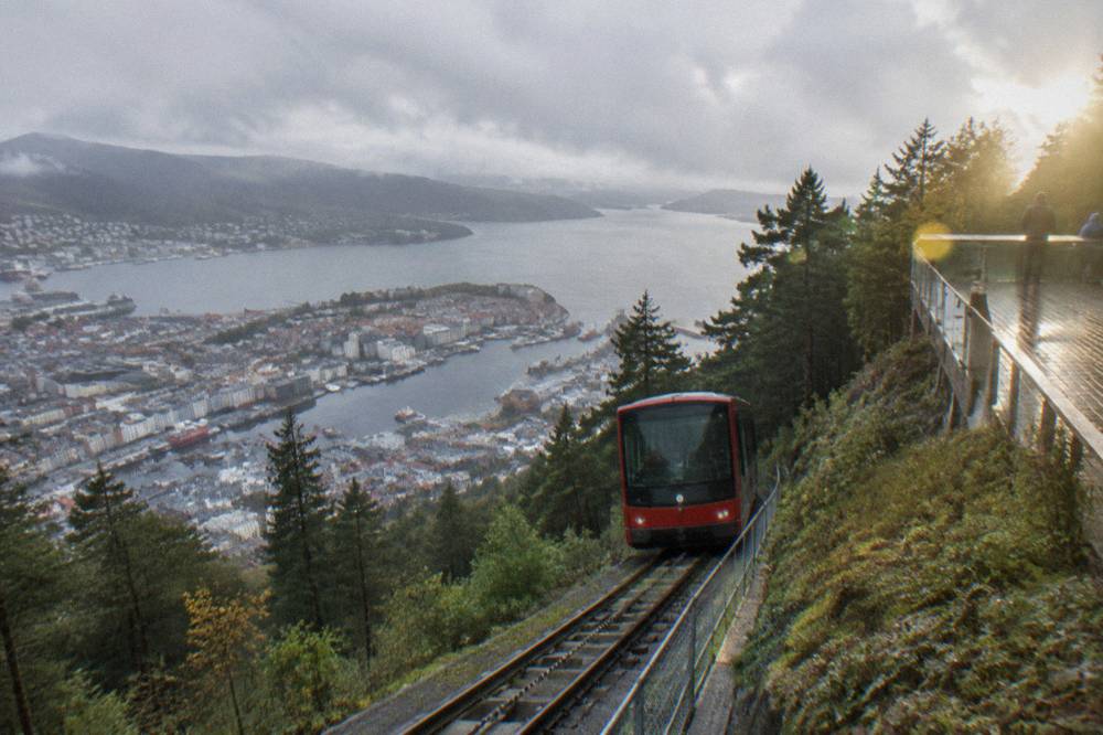 The Fløibanen funicular car climbing the wooded slope of Mount Fløyen above Bergen, with the city and fjord visible below.